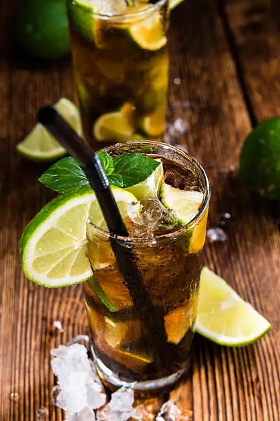 Cold Longdrink (Cuba Libre) with brown rum and fresh lime on rustic wooden background