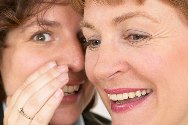 two women whisper a secret stock photo