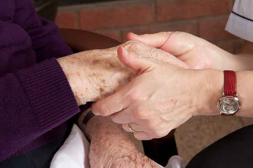Midsection of a nurse holding the hand of an elderly patient who is lying on her bed at home.