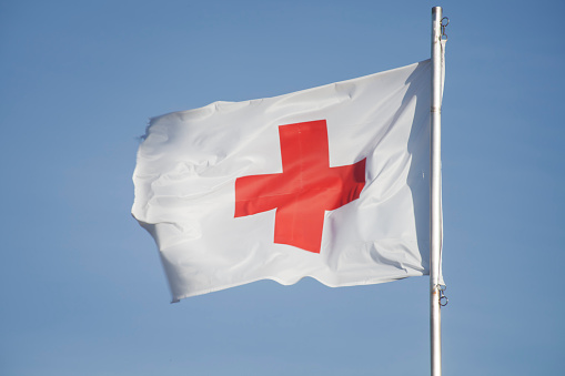 La Coruña, Spain-December 23, 2012: Close up of flag displaying a red cross on white background which is the international symbol for first aid, hanging in the open air outside a small temporary first aid medical service.  Clear blue sky background, evening light .