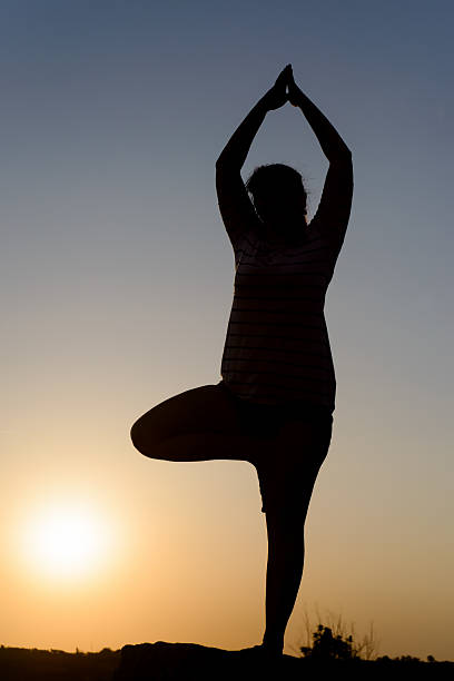 istock Woman practicing yoga silhouetted at sunset 499773720