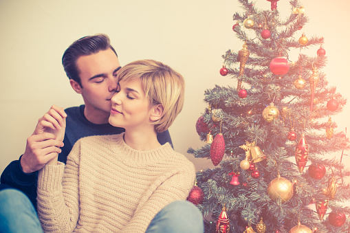 Young couple sitting beside Christmas tree