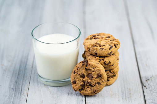 Glass with milk and chocolate chip cookies on wooden background