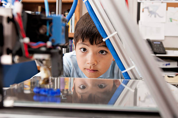 Boy watches machine intently. A young boy watches as a 3D printer prints an object. 3d printing photos stock pictures, royalty-free photos & images