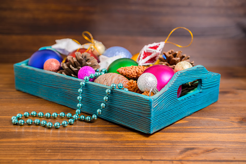composition of retro wooden box with Christmas decoration, tinsel,  pinecones, stars, balls and beads on wooden background, closeup