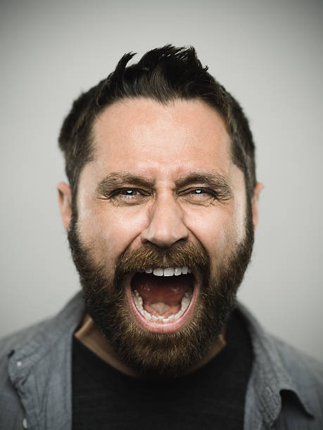 Portrait of a caucasian real young man Portrait of a real caucasian young man with screaming with excited expression looking at camera. Brown eyes and hair with beard. 35 years old north american. Vertical color image from a dslr camera in studio. mouth open human face shouting screaming stock pictures, royalty-free photos & images