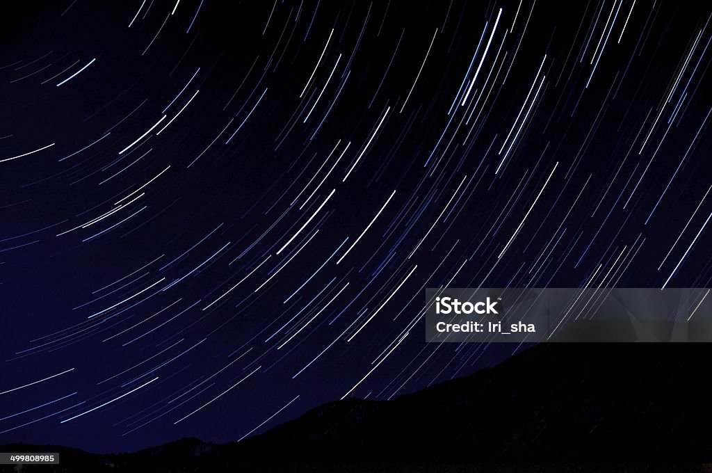 star tracks night sky space Star trails on the sky, shot long exposure, on a background the dark contour of the mountains. Abstract Stock Photo