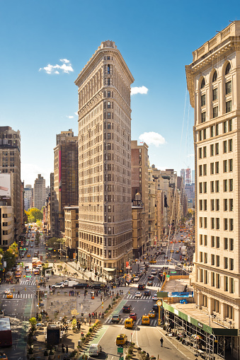 New York City, New York, USA - October 17, 2015: View of midtown Manhattan along Broadway at the historic Flatiron Building with cars and people visible from a distance.  The Flatiron Building is a historic landmark built in 1902.