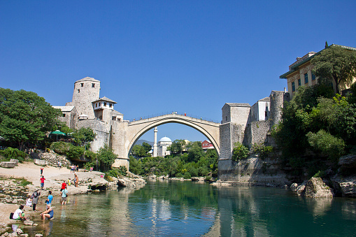 Mostar, Bosnia and Hercegovina - September 1, 2015: Tourists are at the old bridge (Stari Most) in Mostar city at summer time. Renowated old bridge (Stari most) full of tourists over the Neretva river in Mostar as seen from the Cejvan Cehan mosque during tourist season. The bridge was made by ottoman architect Hayreddin.