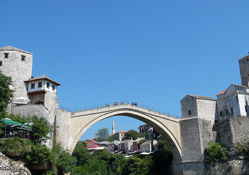 Mostar, Bosnia and Hercegovina - September 1, 2015: Tourists are at the old bridge (Stari Most) in Mostar city at summer time. Renowated old bridge (Stari most) full of tourists over the Neretva river in Mostar as seen from the Cejvan Cehan mosque during tourist season. The bridge was made by ottoman architect Hayreddin.