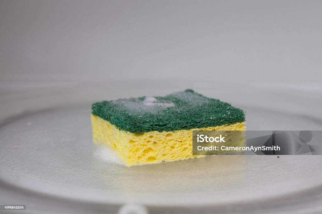 green and yellow sponge in microwave A green and yellow sponge covered in soap suds sits inside of a microwave Cleaning Sponge Stock Photo