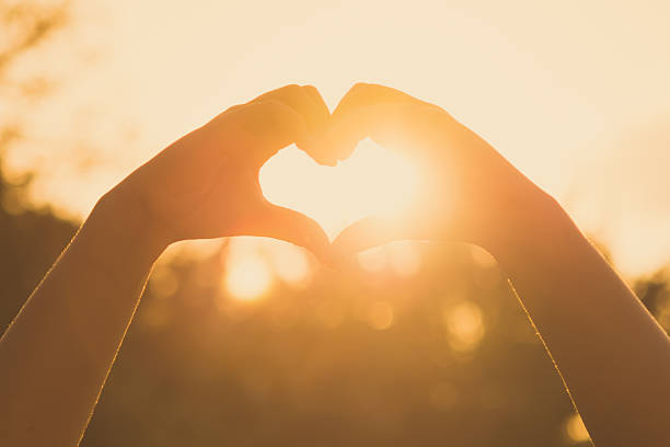 hands forming a heart shape at sunset stock photo