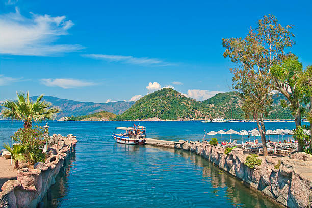 small tourist boat at pier in sea bay small tourist boat at Icmeler pier in Aegean sea bay with palm trees at foeground and mountains at background, Marmaris, Turkey marmaris stock pictures, royalty-free photos & images