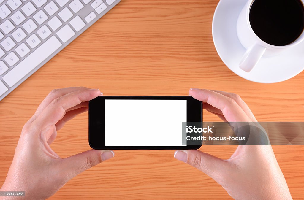 Hands holding touchscreen smart phone at office Hands holding blank white screen smart phone on business desk. Adult Stock Photo