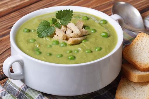 Green pea soup with croutons and mint closeup on a wooden table. horizontal