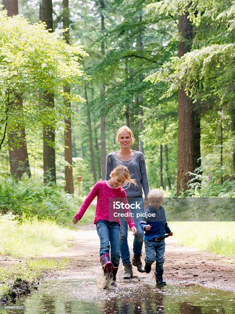 Family walk in the woods Mother looking at camera, children playing in puddle Jumping Stock Photo