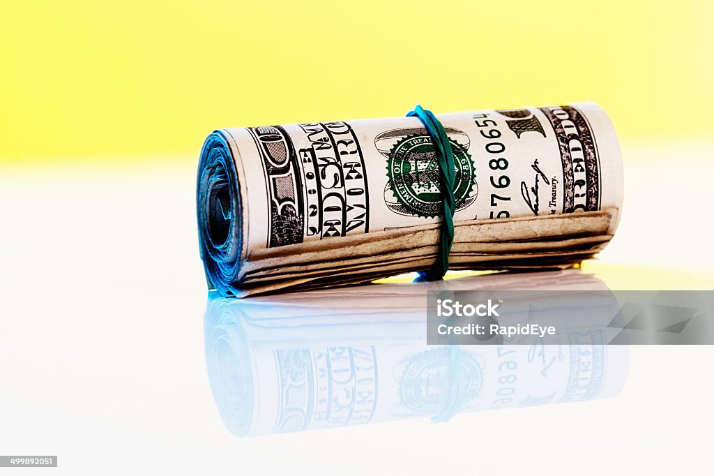 Tightly-wound roll of US one-hundred dollar banknotes A tightly-rolled bundle of one-hundred dollar US banknotes, held by a rubber band. Background with copy space. A stash of cash for those rainy days! American One Hundred Dollar Bill Stock Photo