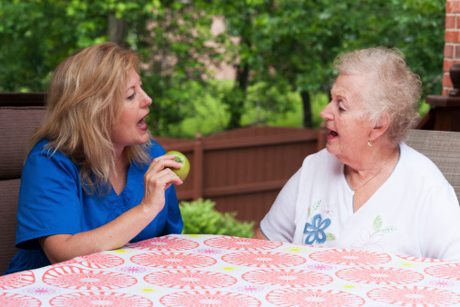 Speech therapist with female stroke patient outdoors during a home health therapy session modeling the production of the A consonant during speech training for apraxia rehabilitation