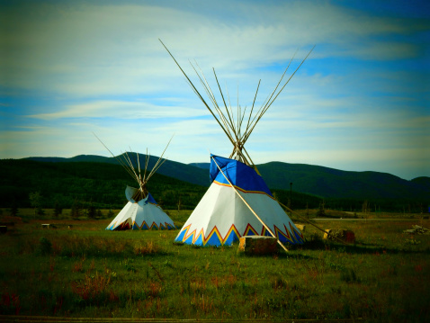 Two majestic teepees sitting in the grasslands of an expansive prairie.