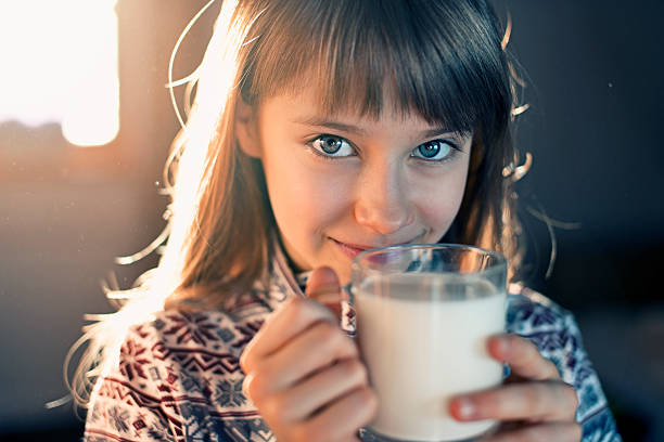 Closeup of 9 year old little girl drinking a glass of milk. The girl is smiling into the camera and is backlit fron the nearby window.