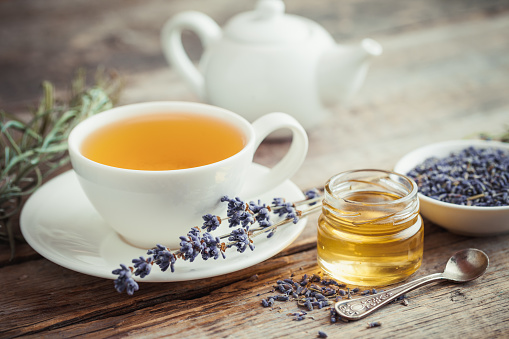 Healthy tea cup, jar of honey, dry lavender flowers and teapot on background. Selective focus. Retro styled.