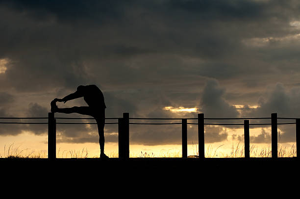 silhouette of an athlete stretching at dusk stock photo