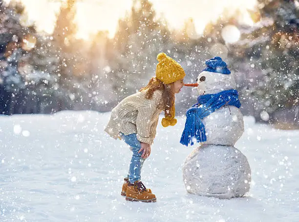 happy child girl plaing with a snowman on a snowy winter walk