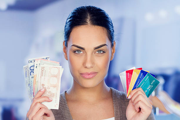 Beautiful young woman over grunge grey wall holding credit card with happy face smiling doing ok sign with hand on eye looking through fingers