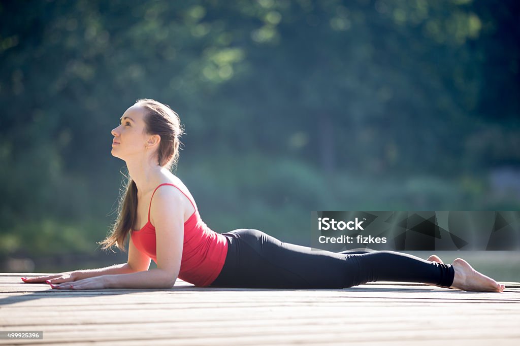 Teenage girl in Sphinx yoga Pose Beautiful sporty fit young woman in sportswear working out outdoors on summer day, doing exercise for back, easy variation of cobra asana, Sphinx Pose or half Cobra posture, full length Activity Stock Photo