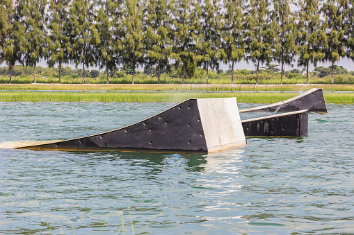 A wakeskater slides across a huge floating rail obstacle behind a boat.