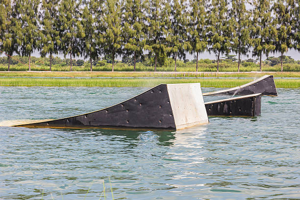 wakeskater slides across a huge floating rail obstacle behind A wakeskater slides across a huge floating rail obstacle behind a boat. jump board stock pictures, royalty-free photos & images