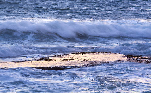 istock Ocean waves splash over calm rock shelf at dawn 499930710