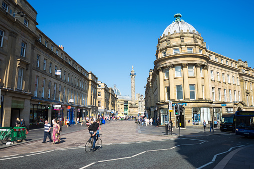 Newcastle Upon Tyne, UK, England - September 10, 2015:  Grey's Monument, Newcastle Upon Tyne. Taken from the head of Grainger street. The sky is blue.  A bike rides across the road, and people are walking along the street.