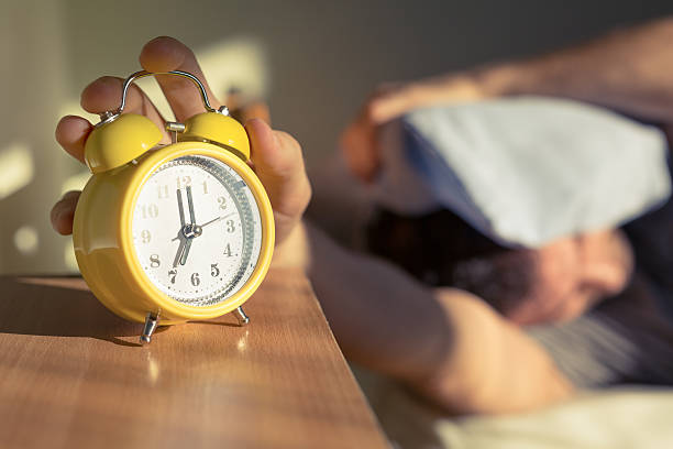 Procrastination Sleeping man disturbed by alarm clock early in the morning. napping stock pictures, royalty-free photos & images