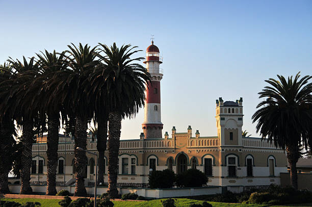 Swakopmund, Namibia - Jul 12, 2019: Red lighthouse, white German fort and row of palms in colonial town of Swakopmund in Namibia