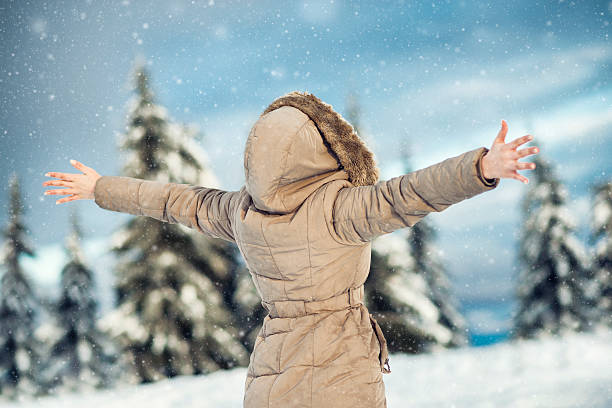 istock Young Woman Enjoying Winter with Raised Arms While Snowing 499954736