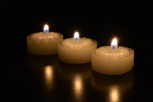 Three tea light candles burning on a dark table