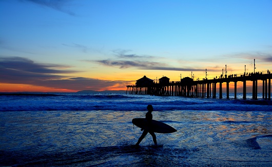Photograph of a surfer silhouetted against a beautiful California sunset and pier. Taken at Huntington Beach, California.