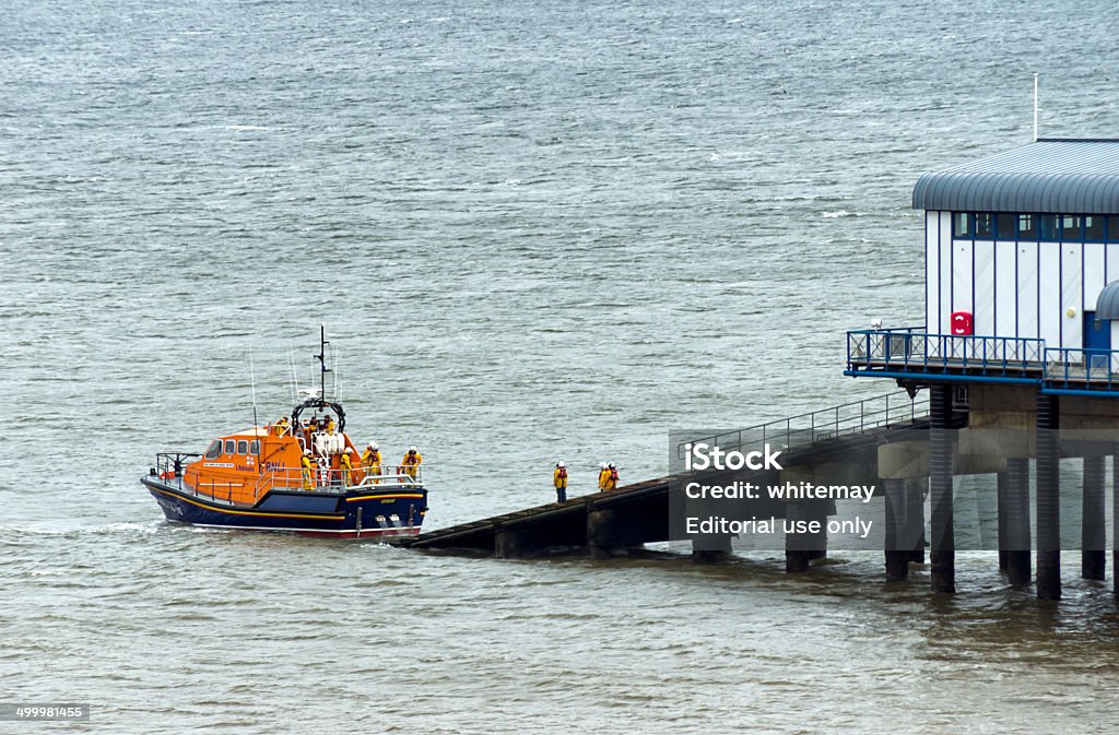 Reversing Cromer lifeboat Cromer, Norfolk, England - May 11, 2014: The lifeboat being reversed towards the slipway which leads from the lifeboat house at the end of the pier in Cromer, Norfolk, in Eastern England on a rainy day. (Background people; overcast day.) Coastline Stock Photo