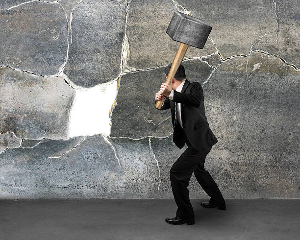 Businessman holding sedgehammer to crack wall stock photo