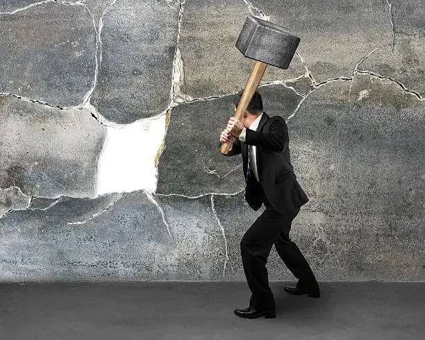 Businessman holding sedgehammer to crack concret wall