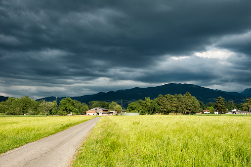 dark clouds over sunny farmland with trees and mountains in the background