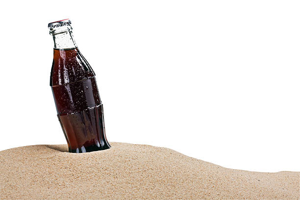 glass bottle of cola in the sand stock photo