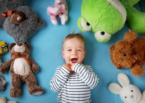 Photo of Happy one year old boy lying with many plush toys