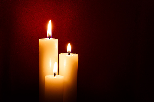 Three candles on a dark red background.