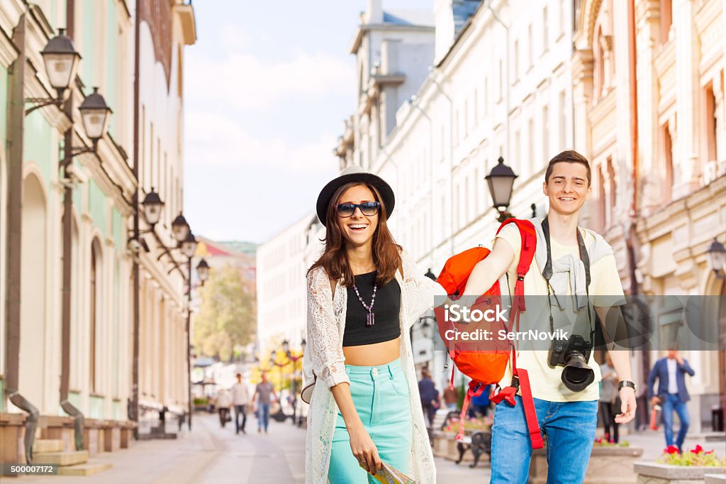 Happy girl holds arm of young man walking forward Happy girl holds arm of young man walking forward on the beautiful street during summer day time Adult Stock Photo