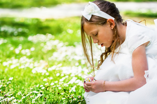 Close up portrait of cute girl in white dress picking flowers.