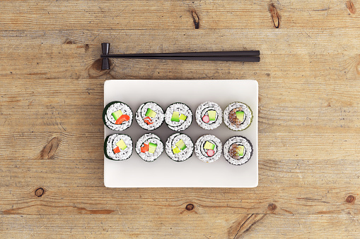 Top view on a plate full with sushi rolls, with chop stick next to it. It is a close up on a wooden table.