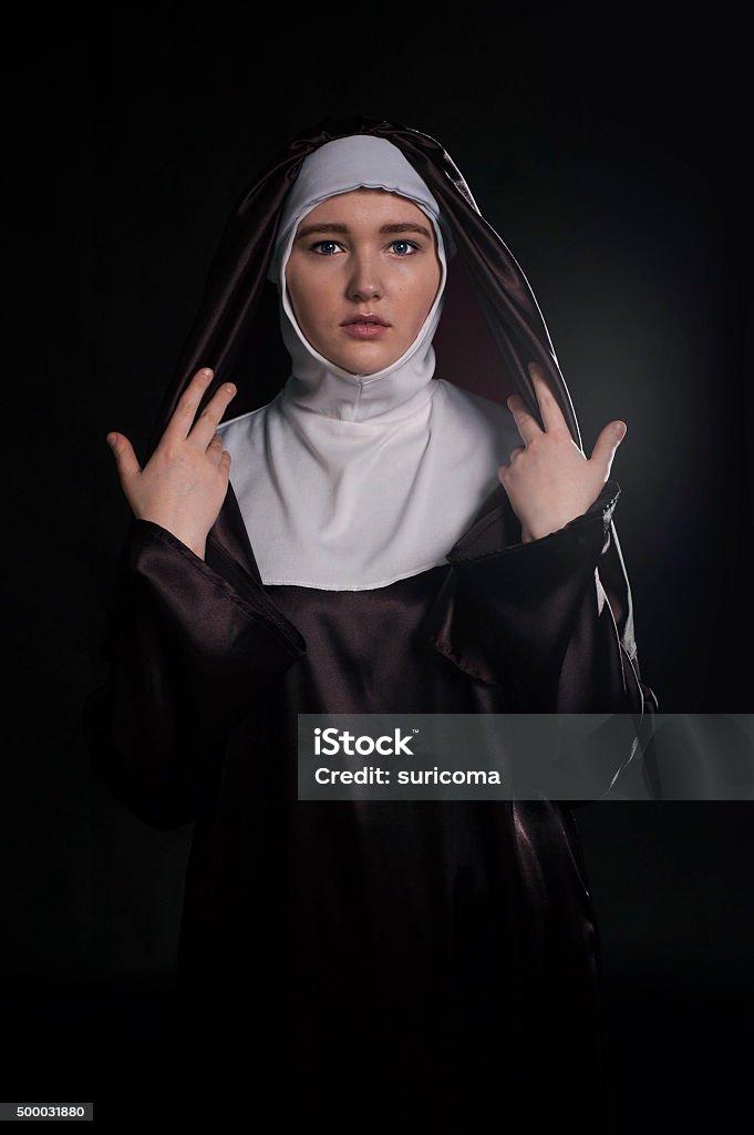Catholic nun Front portrait of the young beautiful nun. Low key lighting. On black. 2015 Stock Photo