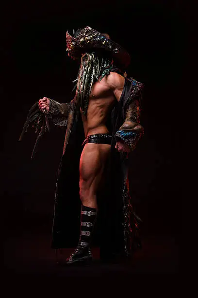 Man with sexy strong muscular body dressed in a costume monster, octopus mask and beard of tentacles. Studio photography, on dark background . 
